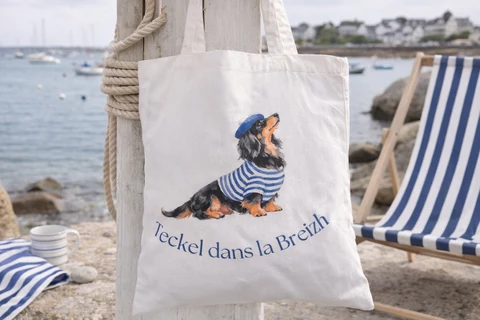 Tote bag blanc avec illustration d’un teckel à poil long en haut rayé bleu et blanc, béret bleu et texte « Teckel dans la Breizh ».