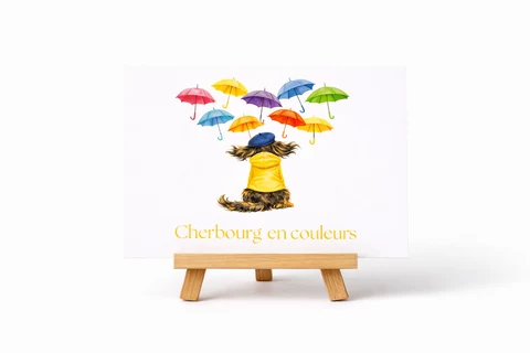 Carte illustrée avec une petite silhouette de chien vue de dos, vêtue de jaune et coiffée de bleu, sous des parapluies colorés et le titre Cherbourg en couleurs.
